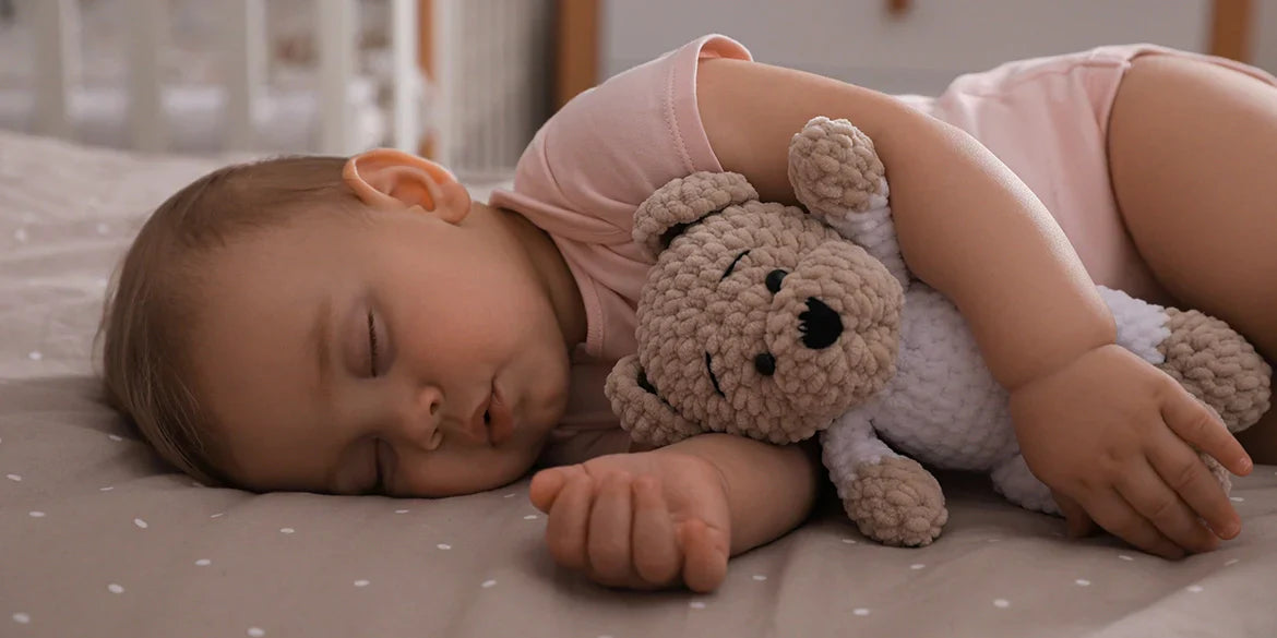 Baby schläft mit gehäkeltem Teddy im Arm