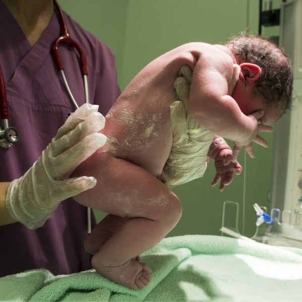 Hebamme hält Neugeborenes hoch nach der Geburt