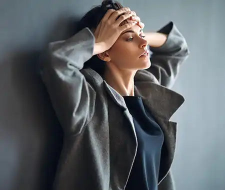 Frau mit Händen am Kopf an die Wand gelehnt