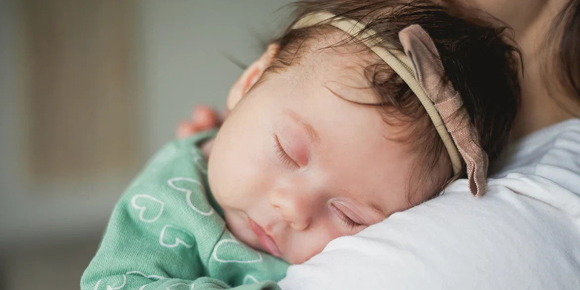 Baby schläft auf Arm der Mutter und trägt Schleifenhaarreif